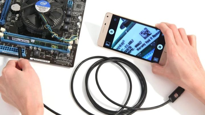 Borescope snake camera inspecting a motherboard, live HD feed shown on smartphone screen