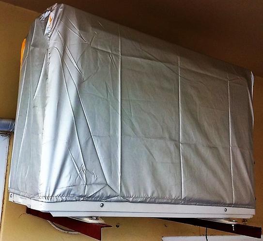 Silver waterproof dust cover fully wrapped around a wall-mounted AC outdoor compressor unit, side view