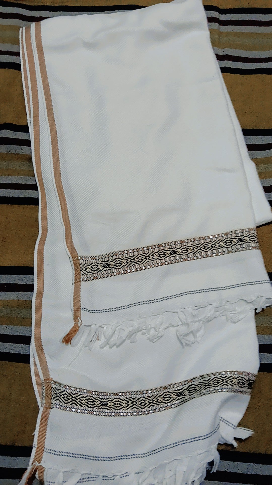 Folded white winter shawl showing the brown woven border pattern and fringed ends